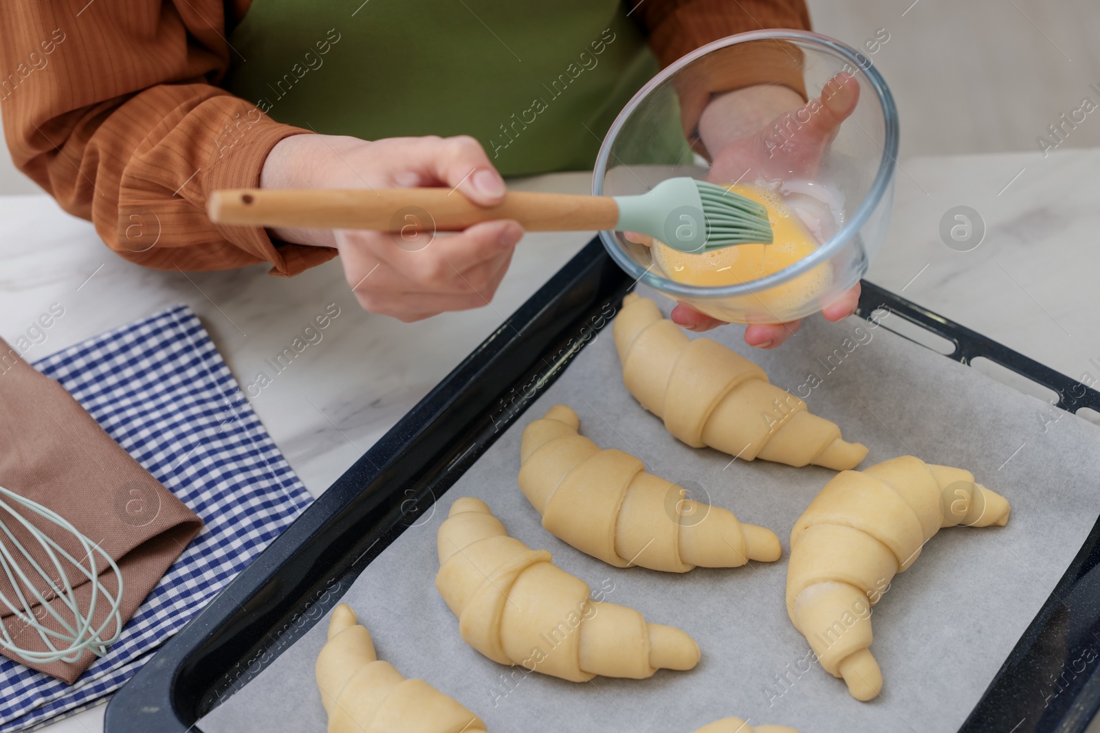 Woman brushing egg wash onto raw croissants at white marble table, closeup Photo of Woman brushing egg wash onto raw croissants at white marble table, closeup