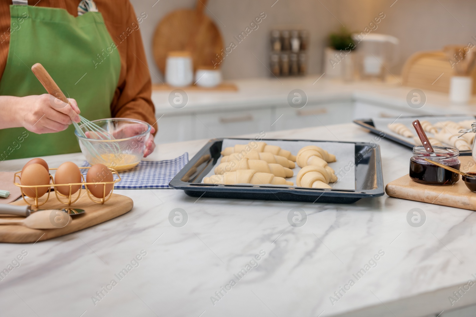 Woman whisking egg wash near raw croissants at white marble table in kitchen, closeup Photo of Woman whisking egg wash near raw croissants at white marble table in kitchen, closeup