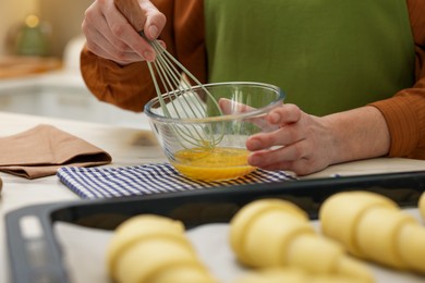 Photo of Woman whisking egg wash near raw croissants at white table indoors, selective focus