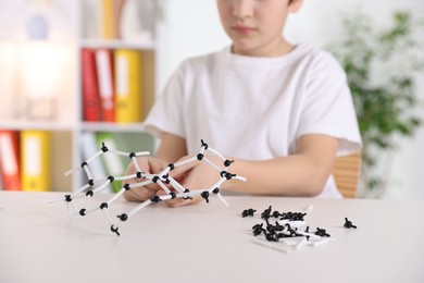 Boy making DNA structure model at desk indoors, closeup