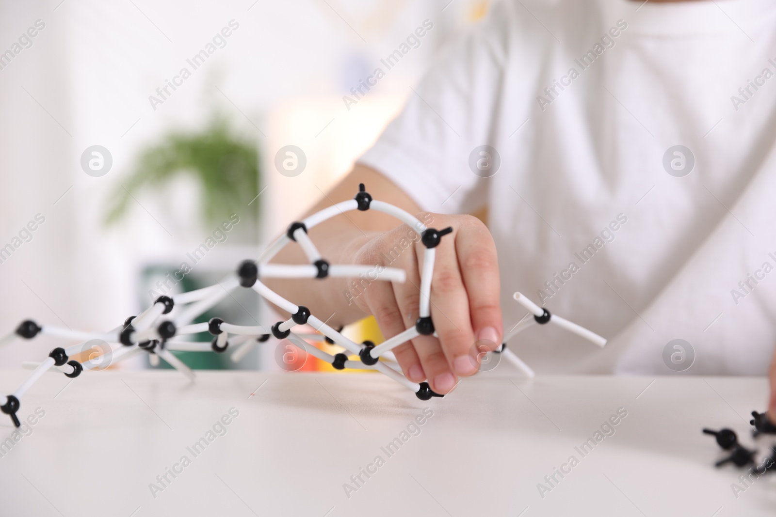 Photo of Boy making DNA structure model at desk indoors, closeup. Space for text