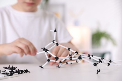 Boy making DNA structure model at desk indoors, closeup. Space for text