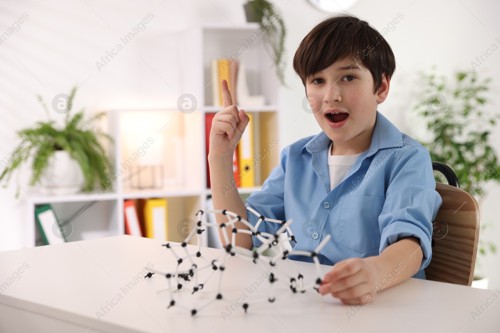 Photo of Boy making DNA structure model at desk indoors. Space for text