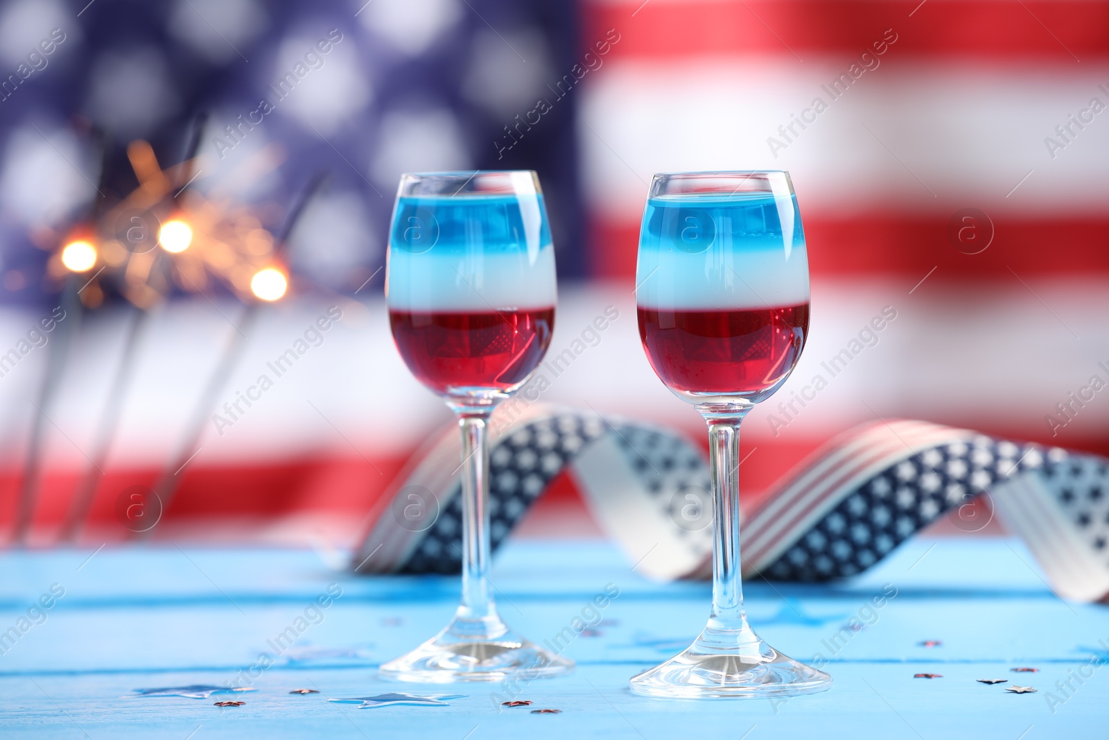 Photo of Tasty cocktail in glasses on light blue wooden table against flag of USA, space for text