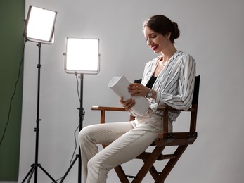 Photo of Beautiful woman with script sitting in director's chair in studio