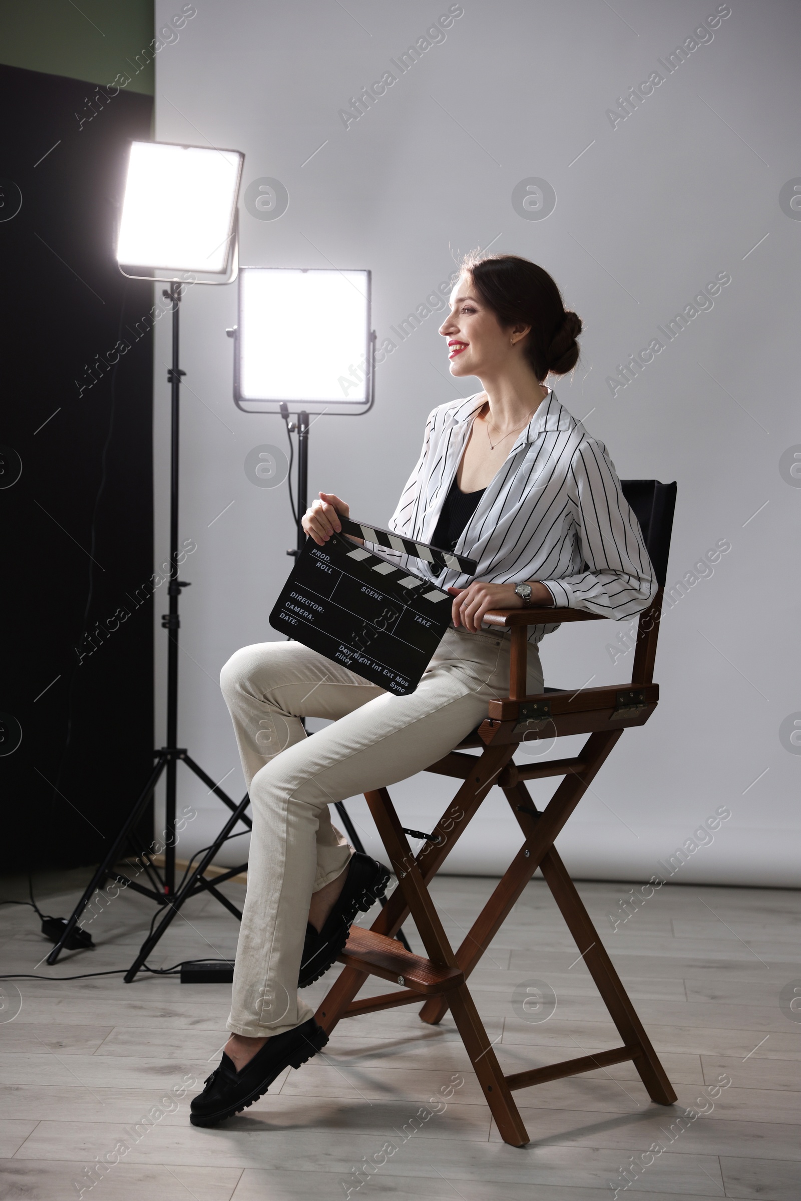 Photo of Beautiful woman with clapperboard sitting in director's chair in studio