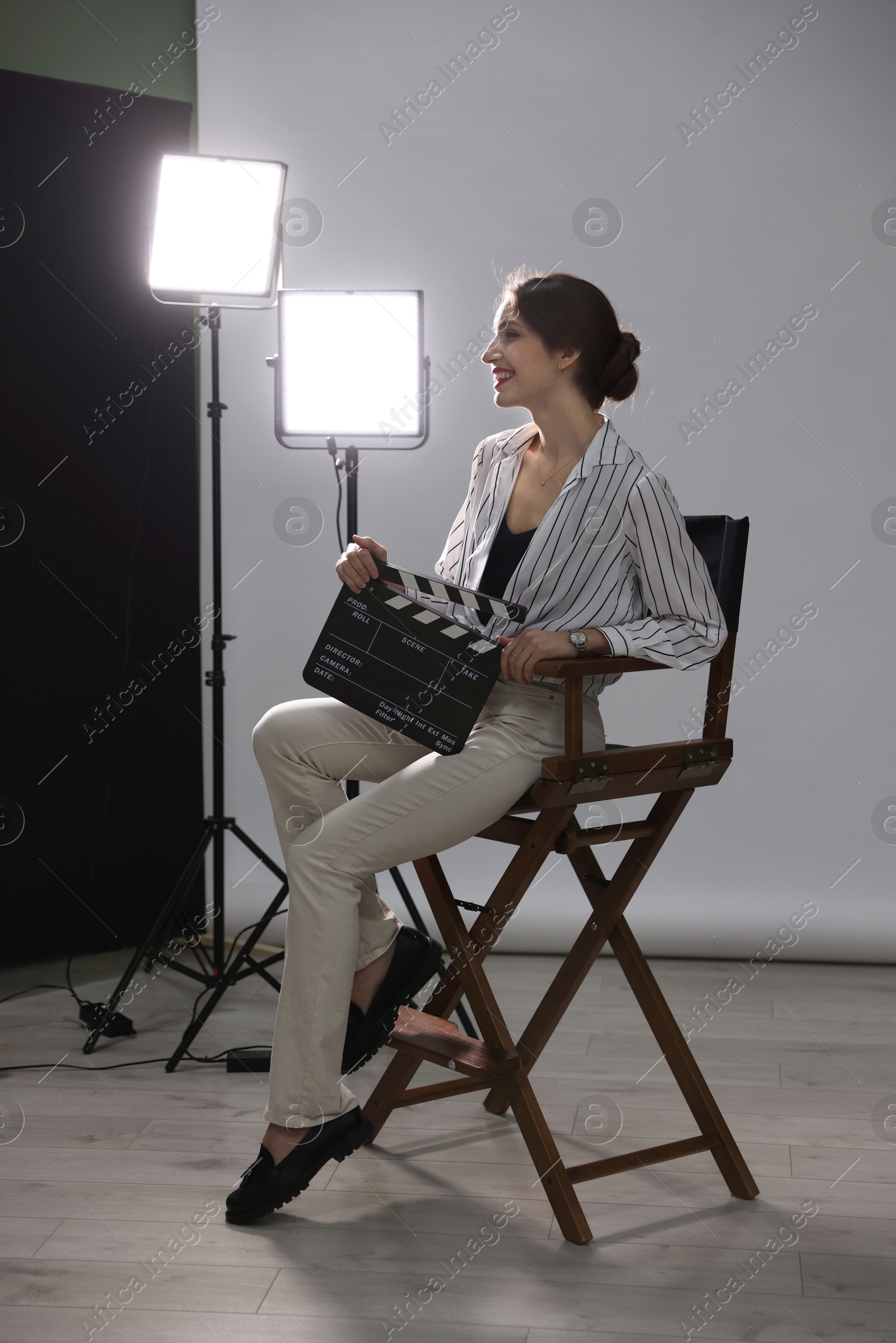 Photo of Beautiful woman with clapperboard sitting in director's chair in studio