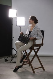 Beautiful woman with clapperboard sitting in director's chair in studio