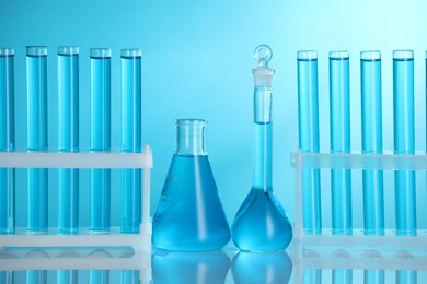 Photo of Laboratory glassware with liquid on mirror surface against blue background