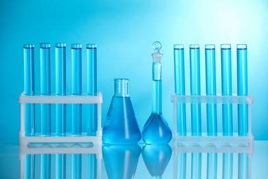 Photo of Laboratory glassware with liquid on mirror surface against blue background