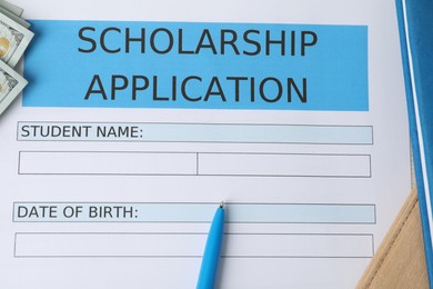 Photo of Scholarship application form, pen, dollar banknotes and book on table, top view