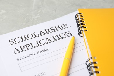 Photo of Scholarship application form, notebooks and pen on grey marble table, closeup