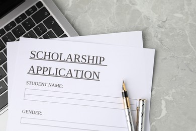 Photo of Scholarship application form, fountain pen and laptop on grey marble table, top view