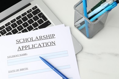 Photo of Scholarship application form, pens and laptop on white marble table, above view