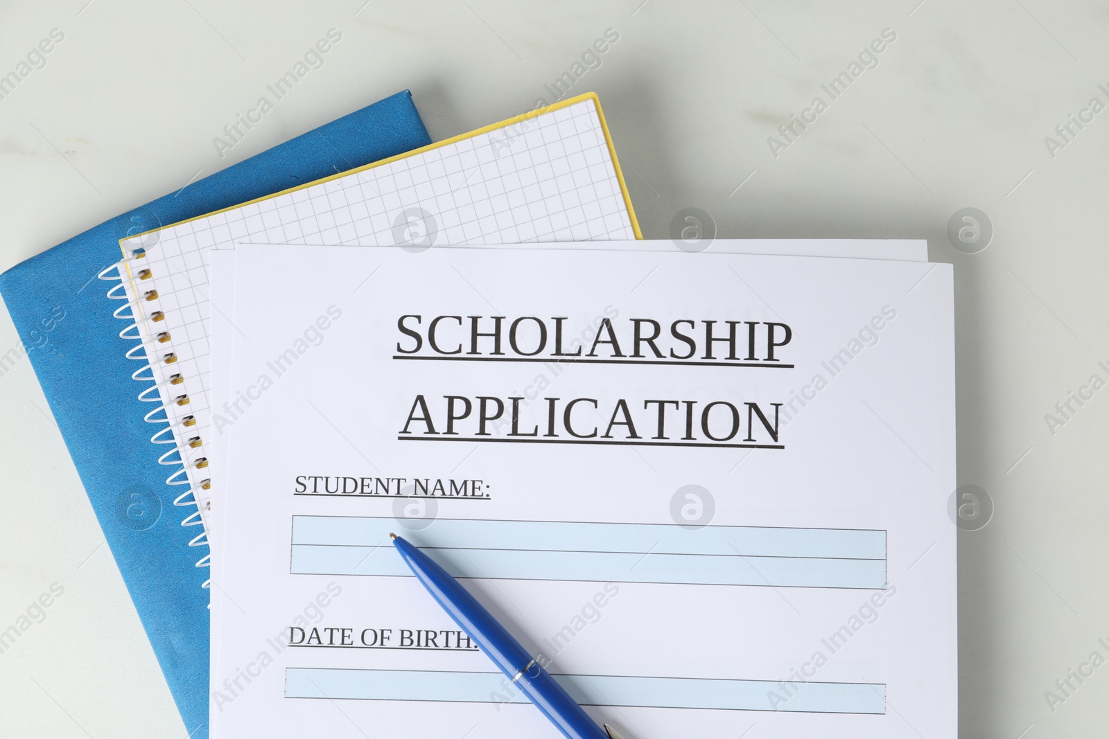 Photo of Scholarship application form, pen and notebooks on white marble table, top view