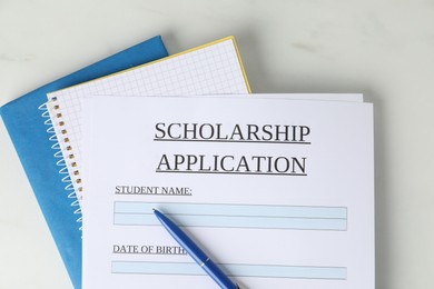 Photo of Scholarship application form, pen and notebooks on white marble table, top view