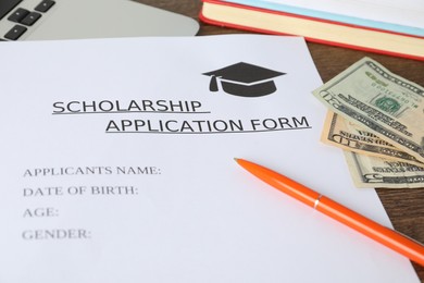 Photo of Scholarship application form, pen, laptop, books and dollar banknotes on wooden table, closeup