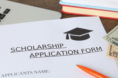 Photo of Scholarship application form, pen, laptop, books and dollar banknotes on table, closeup