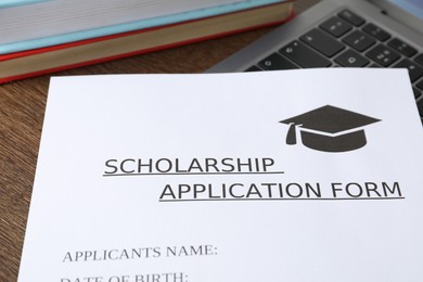 Photo of Scholarship application form, laptop and books on wooden table, closeup