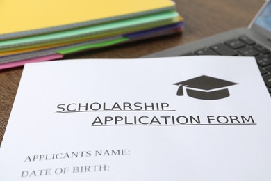 Photo of Scholarship application form, notebooks and laptop on table, closeup