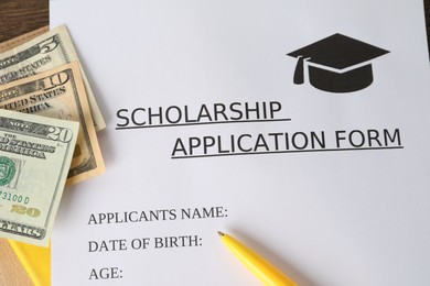 Photo of Scholarship application form, pen and dollar banknotes on table, flat lay