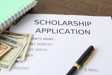 Photo of Scholarship application form, pen, dollar banknotes and notebooks on wooden table, closeup