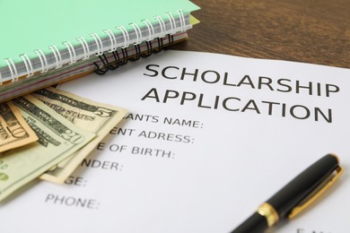 Scholarship application form, pen, dollar banknotes and notebooks on wooden table, closeup