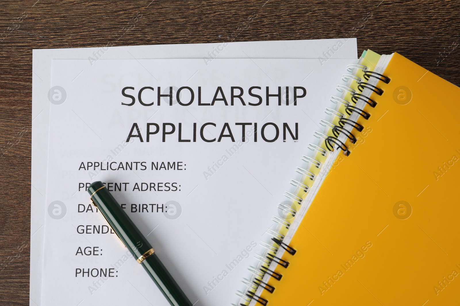 Photo of Scholarship application form, pen and notebooks on wooden table, flat lay