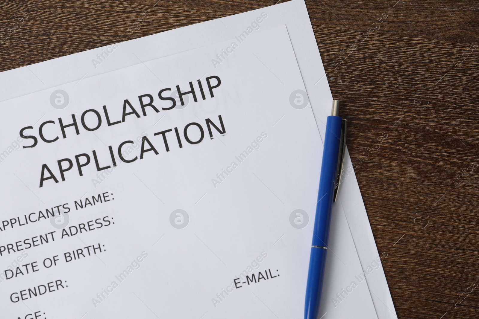 Photo of Scholarship application form and pen on wooden table, top view