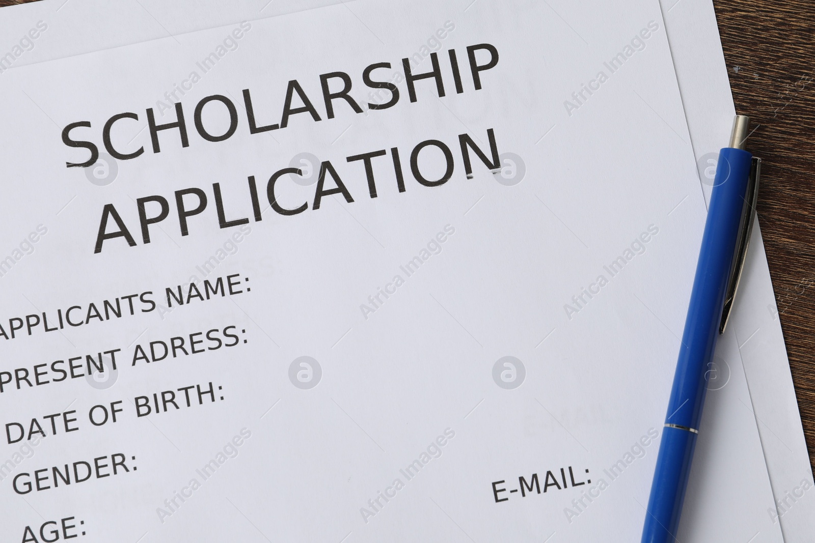 Photo of Scholarship application form and pen on wooden table, top view