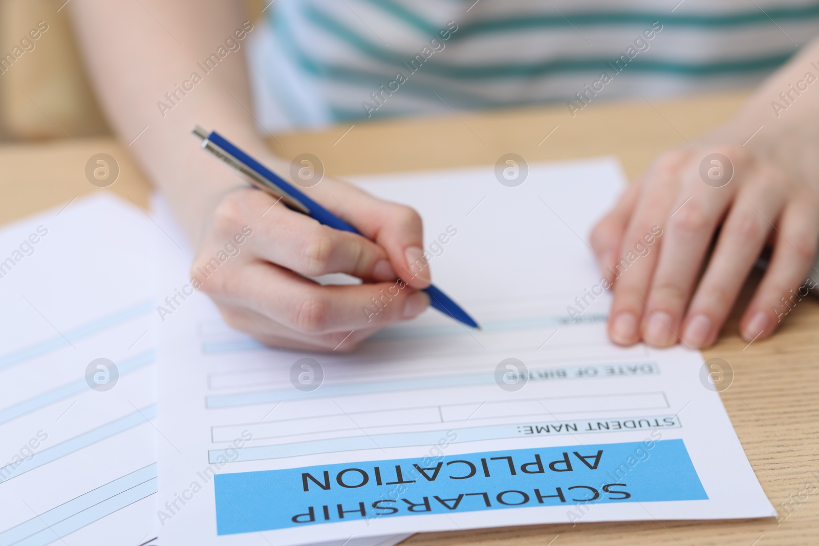 Photo of Student filling scholarship application form at wooden table, closeup