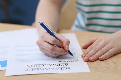 Photo of Student filling scholarship application form at wooden table, closeup