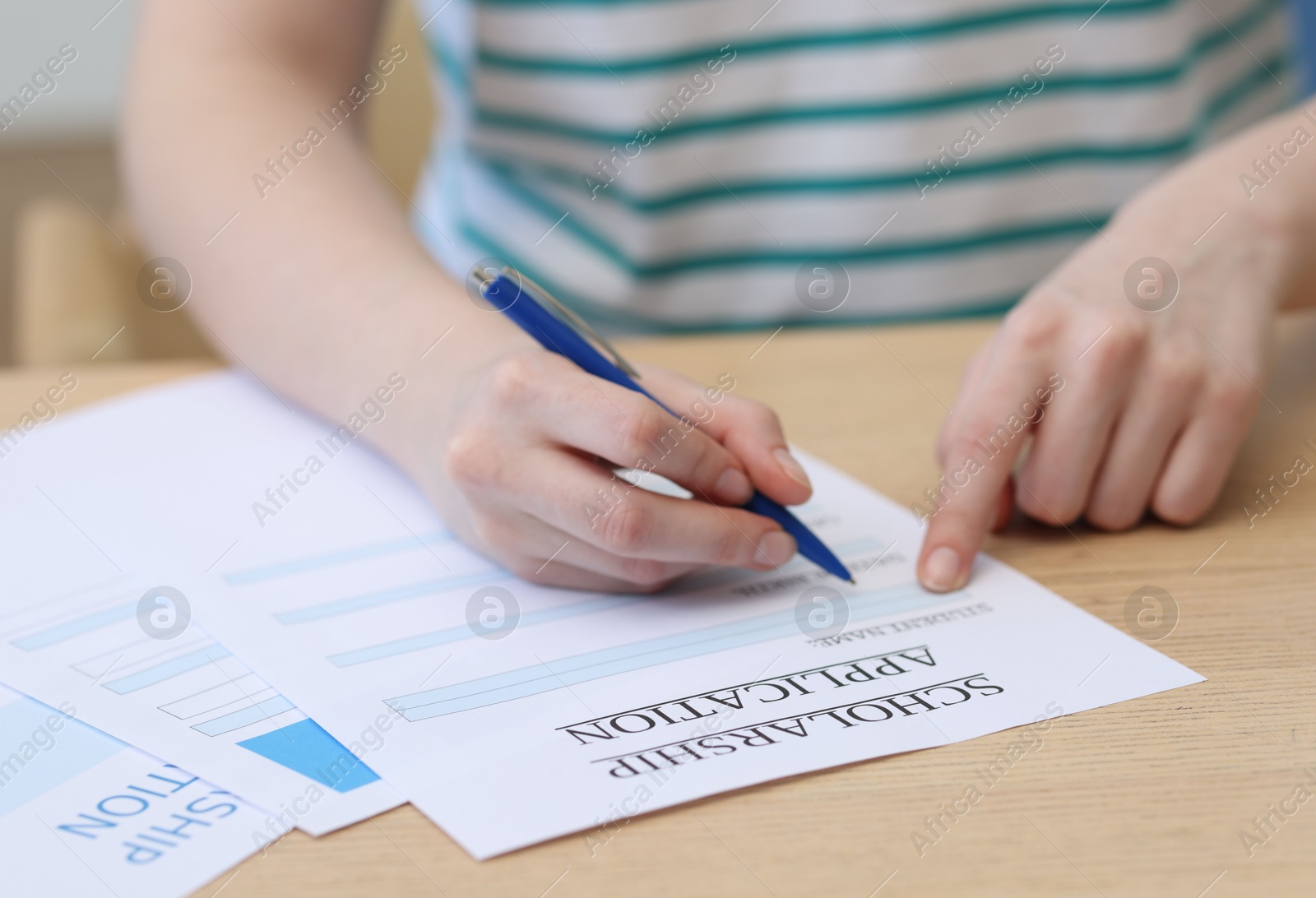 Photo of Student filling scholarship application form at wooden table, closeup