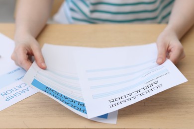 Photo of Student with scholarship application forms at wooden table, closeup