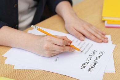 Photo of Student filling scholarship application form at wooden table, closeup