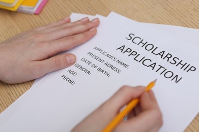 Photo of Student filling scholarship application form at wooden table, closeup