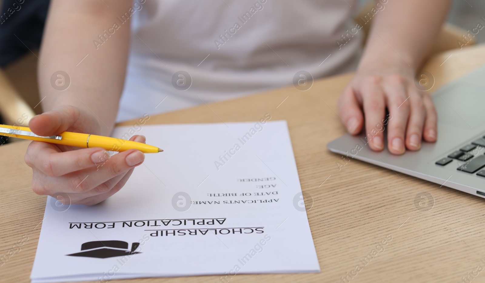 Photo of Student filling scholarship application form at wooden table, closeup