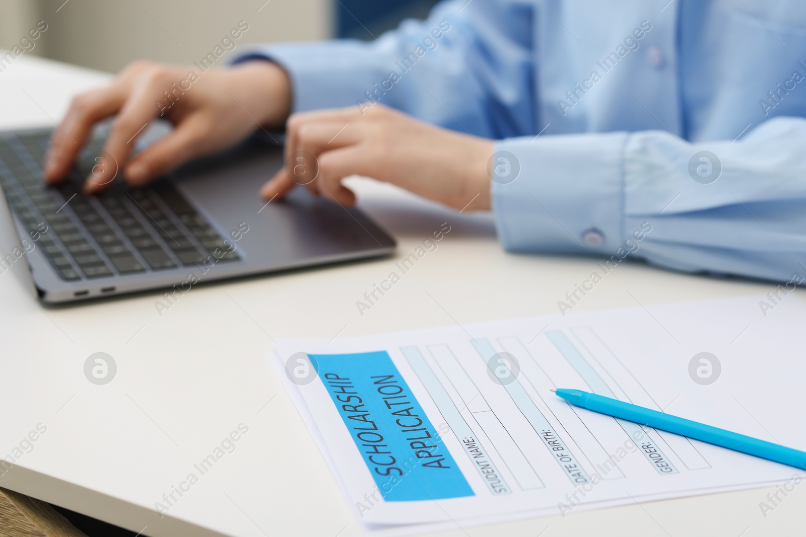 Photo of Student using laptop at white table, focus on scholarship application form and pen