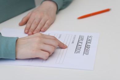 Student with scholarship application form at white table, closeup