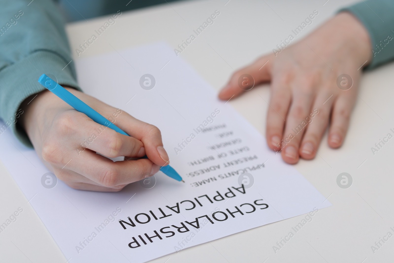 Photo of Student filling scholarship application form at white table, closeup