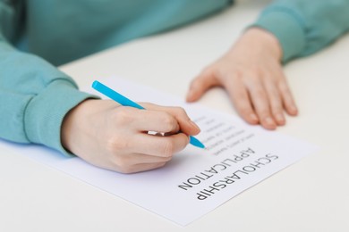 Photo of Student filling scholarship application form at white table, closeup