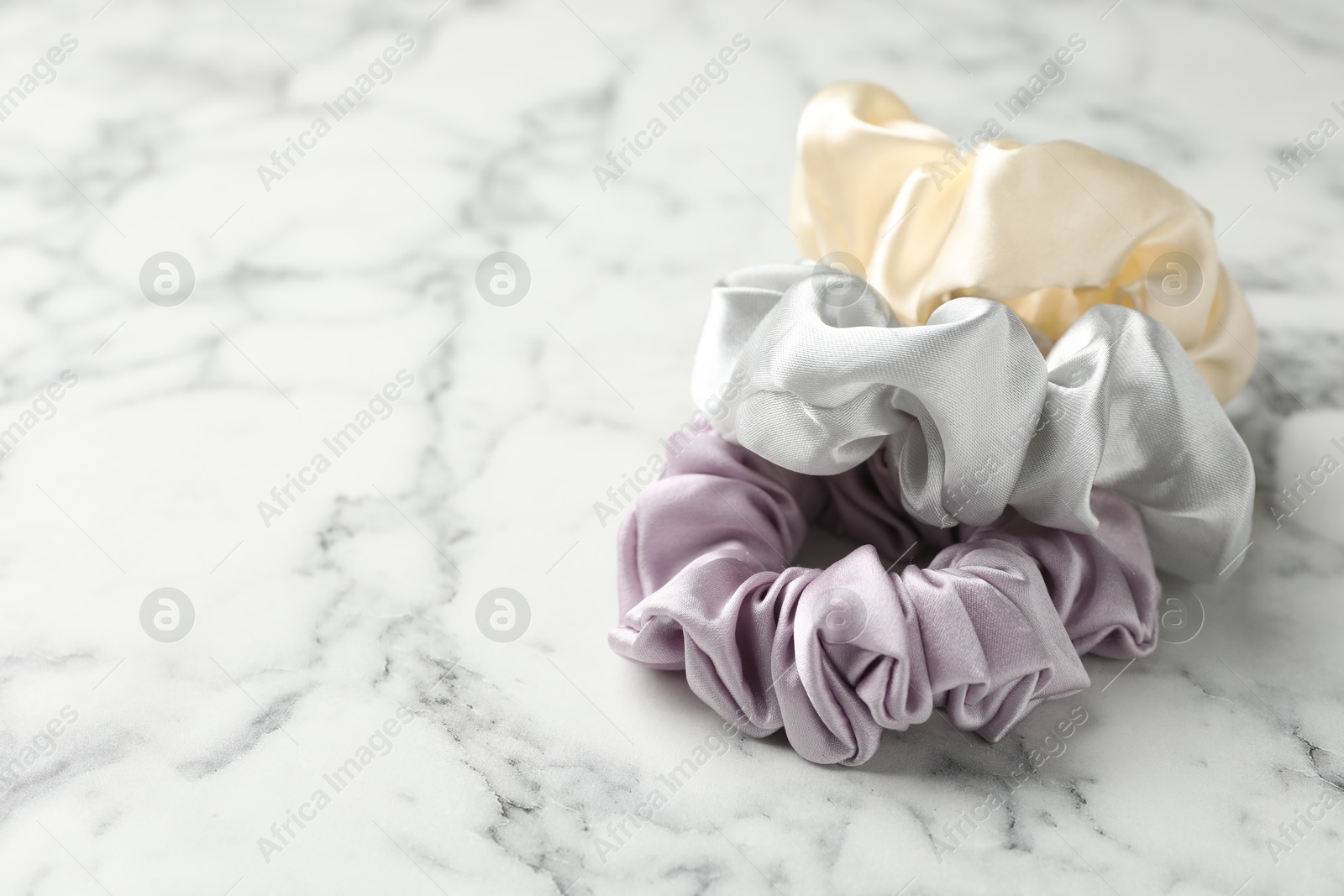 Photo of Different hair scrunchies on white marble table, closeup. Space for text