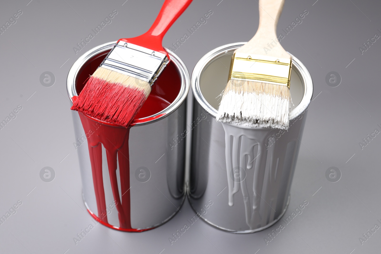 Photo of Cans of paint and brushes on grey background, closeup