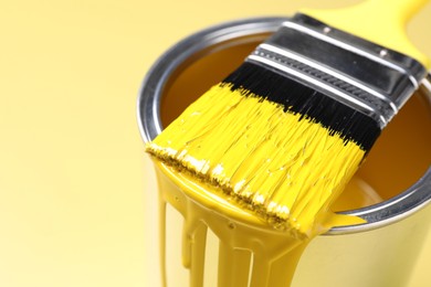 Photo of Can of paint and brush on yellow background, closeup