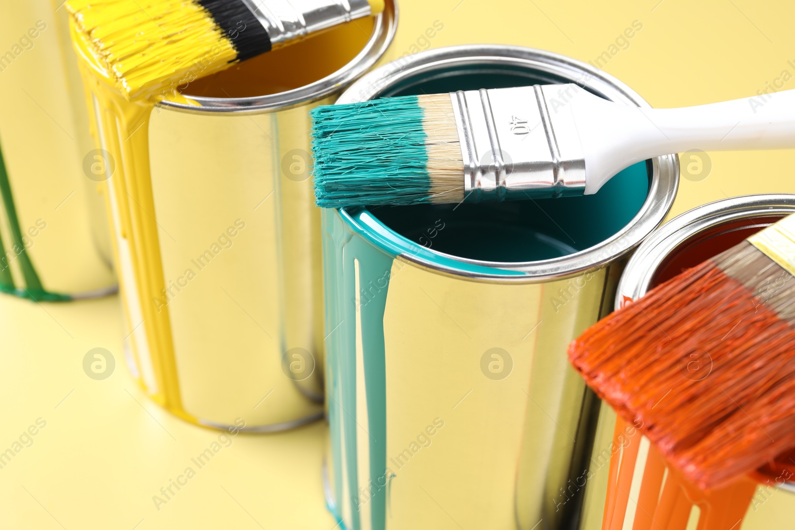 Photo of Cans of paint and brushes on yellow background, closeup