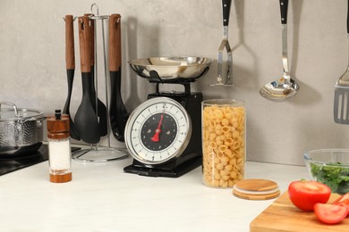 Photo of Retro mechanical kitchen scale, other utensils and different food products on white marble countertop indoors