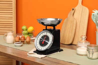 Photo of Kitchen scale, products and cooking utensils on wooden table