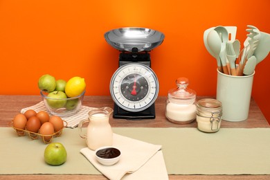 Photo of Kitchen scale, products and cooking utensils on wooden table