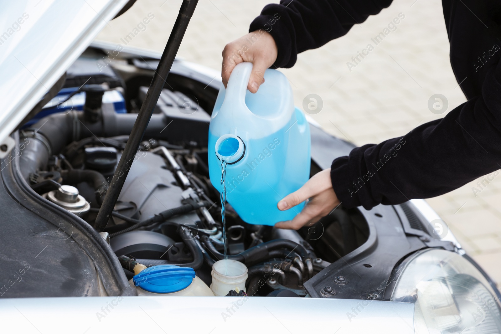 Photo of Man pouring windshield washer from plastic canister into car reservoir outdoors, closeup