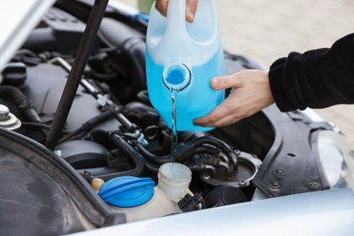 Photo of Man pouring windshield washer from plastic canister into car reservoir outdoors, closeup